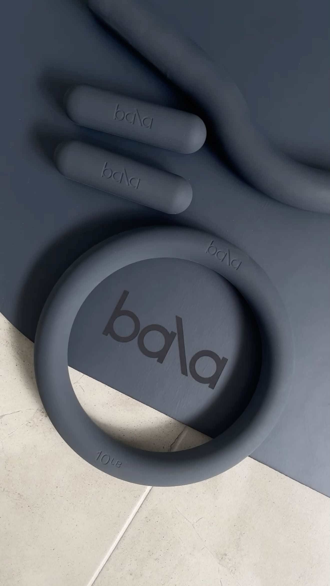 Minimalist Bala pilates equipment including weights and rings on a light-toned floor with soft natural lighting